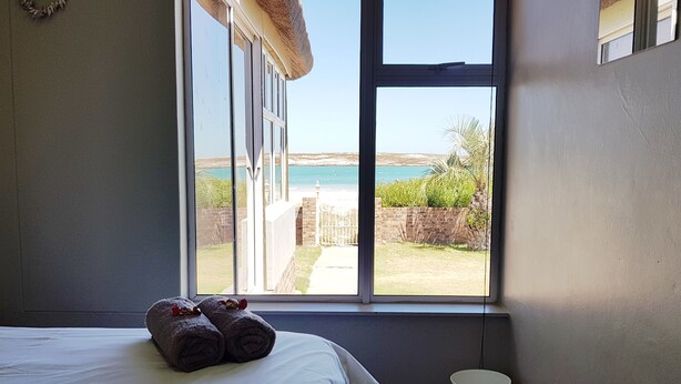 A bedroom with a large window overlooking a beach and a garden. - Seemansrust, Langebaan 9-sleeper (Langebaan)