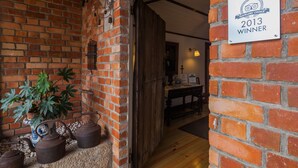 Un mur de briques orné d’une plaque indiquant un prix décerné par TripAdvisor, une porte en bois et un pot de fleurs.
