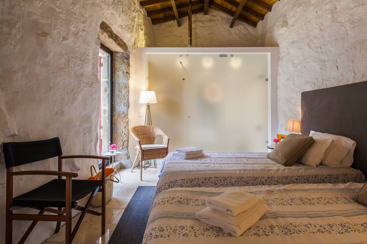 Un dormitorio con cama, una silla, una lámpara y vistas al baño.