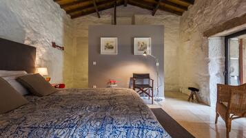 Un dormitorio con una cama grande, techo de madera, una mesita con lámpara y dos cuadros en la pared.