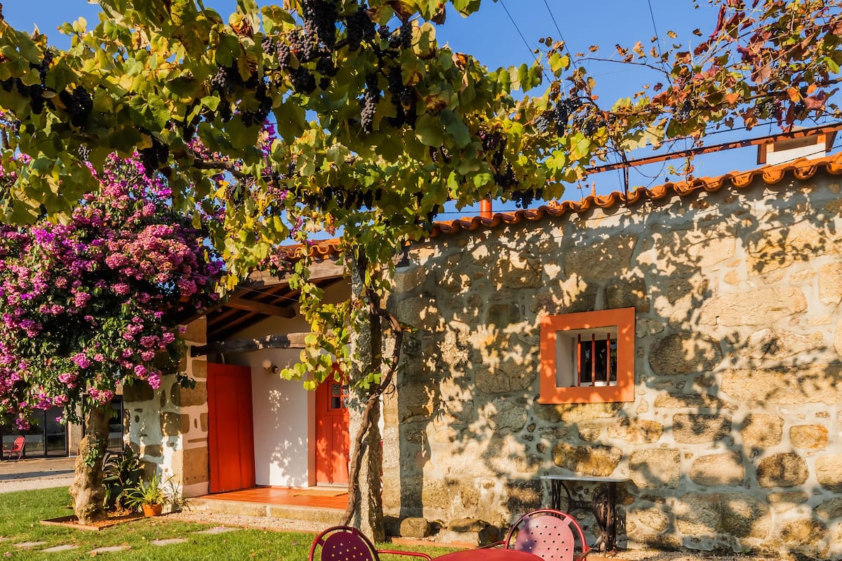 Un edificio de piedra con una puerta roja, una ventana pequeña y una mesa con sillas al frente.