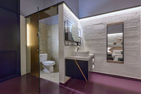 Un baño moderno con cabina de ducha de vidrio, inodoro blanco, lavamanos con espejo y pared con textura.