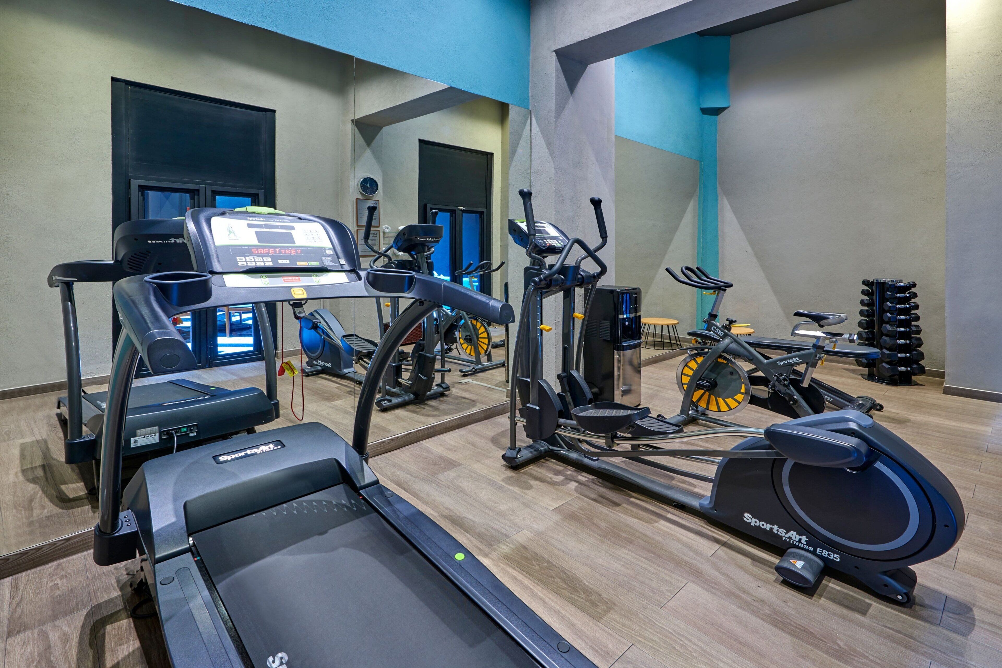Un gimnasio con diversos equipos de ejercicio, incluyendo cintas de correr, elípticas y bicicletas estáticas.