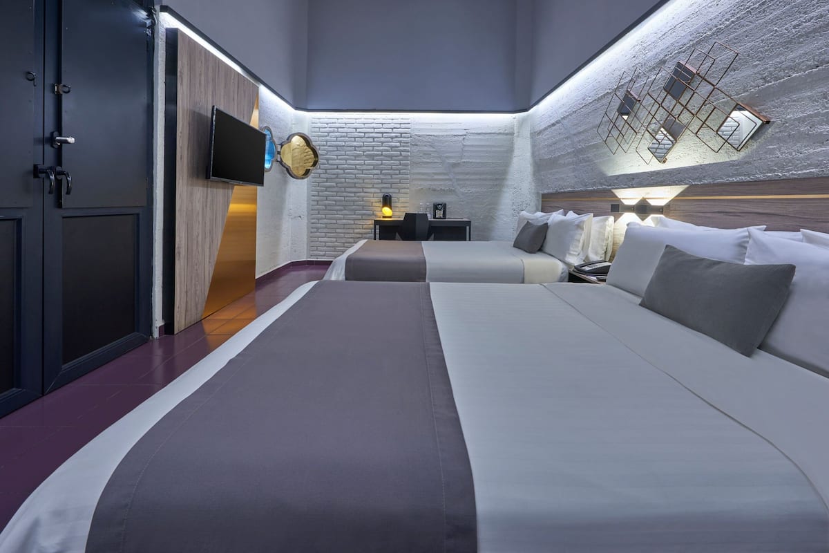 A modern hotel room with a large bed, a desk with a chair, a flat-screen TV, and a unique ceiling design.