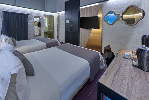 A hotel room with two beds, a desk with a coffee maker, a TV, and a mirror with a unique design.