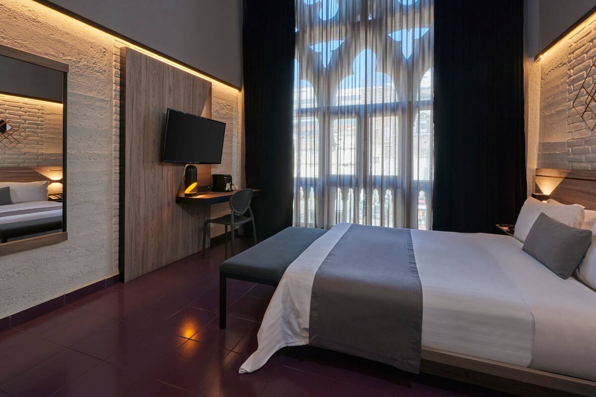 A modern hotel room with a large bed, a desk, and a TV mounted on the wall.