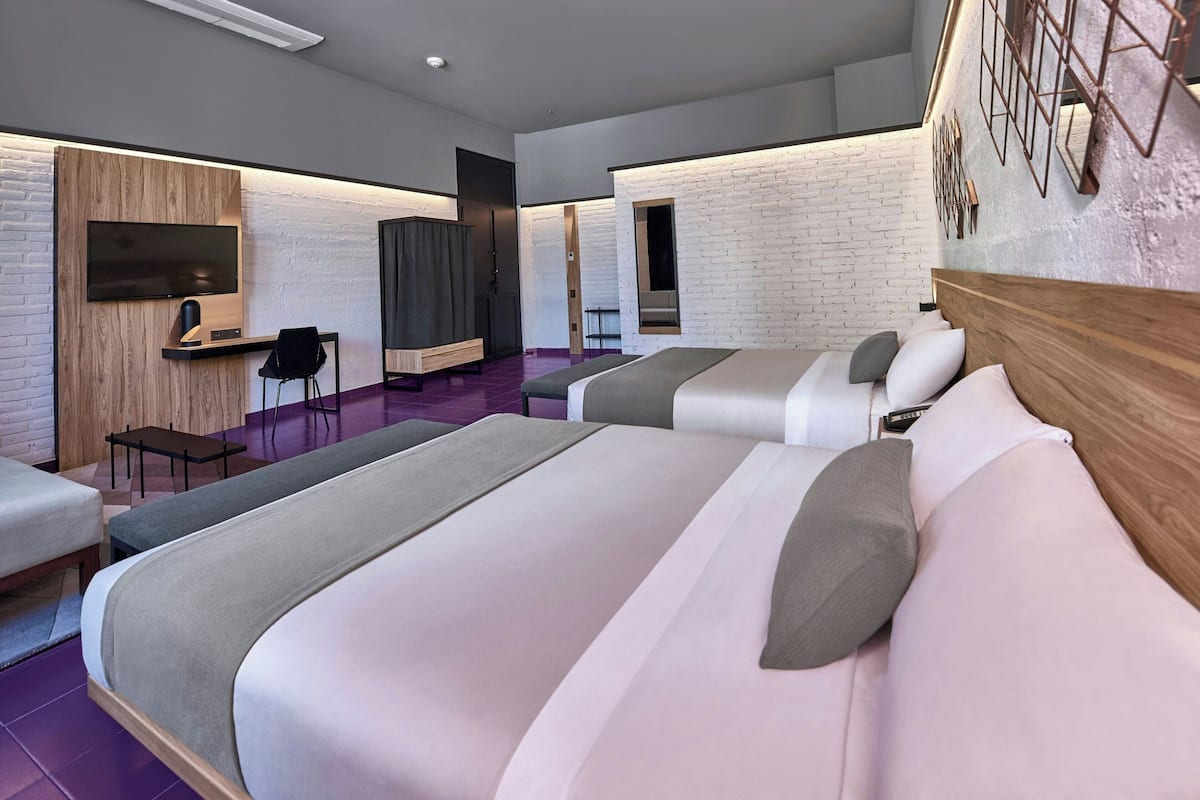 A modern hotel room with three beds, a desk, and a TV.