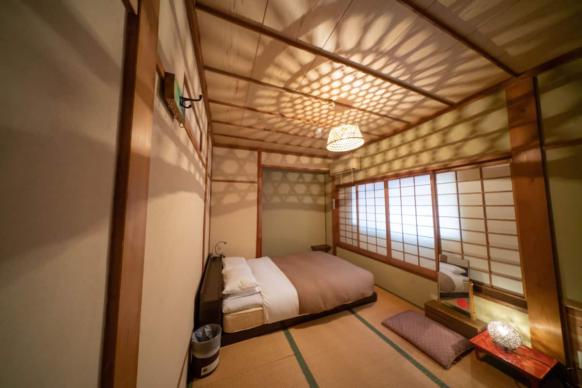 Perinteinen japanilaistyylinen makuuhuone, jossa on tatamimatto, matala sänky, futon-patja ja shoji-tyylinen liukuovi.