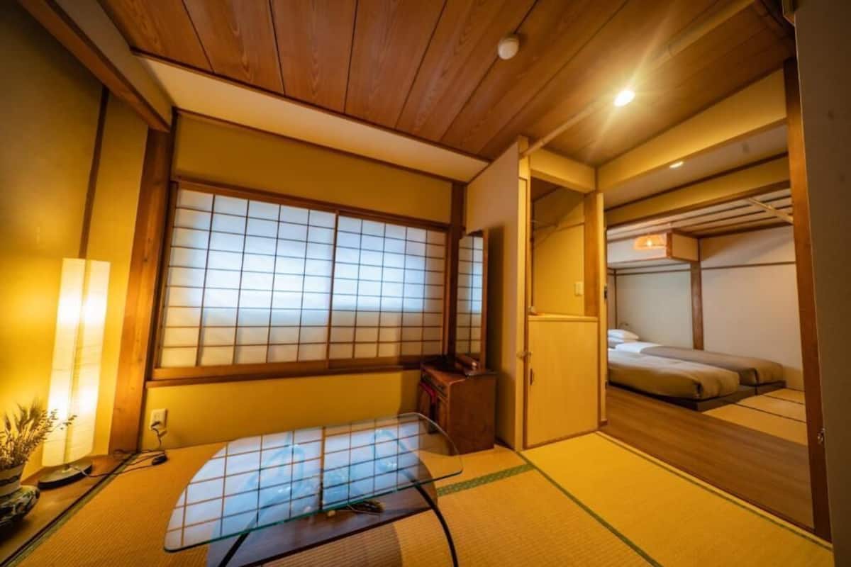 Perinteinen japanilainen huone, jossa on tatamimatto, futon-patja, shoji-liukuovi ja pieni pöytä, jossa on lamppu.