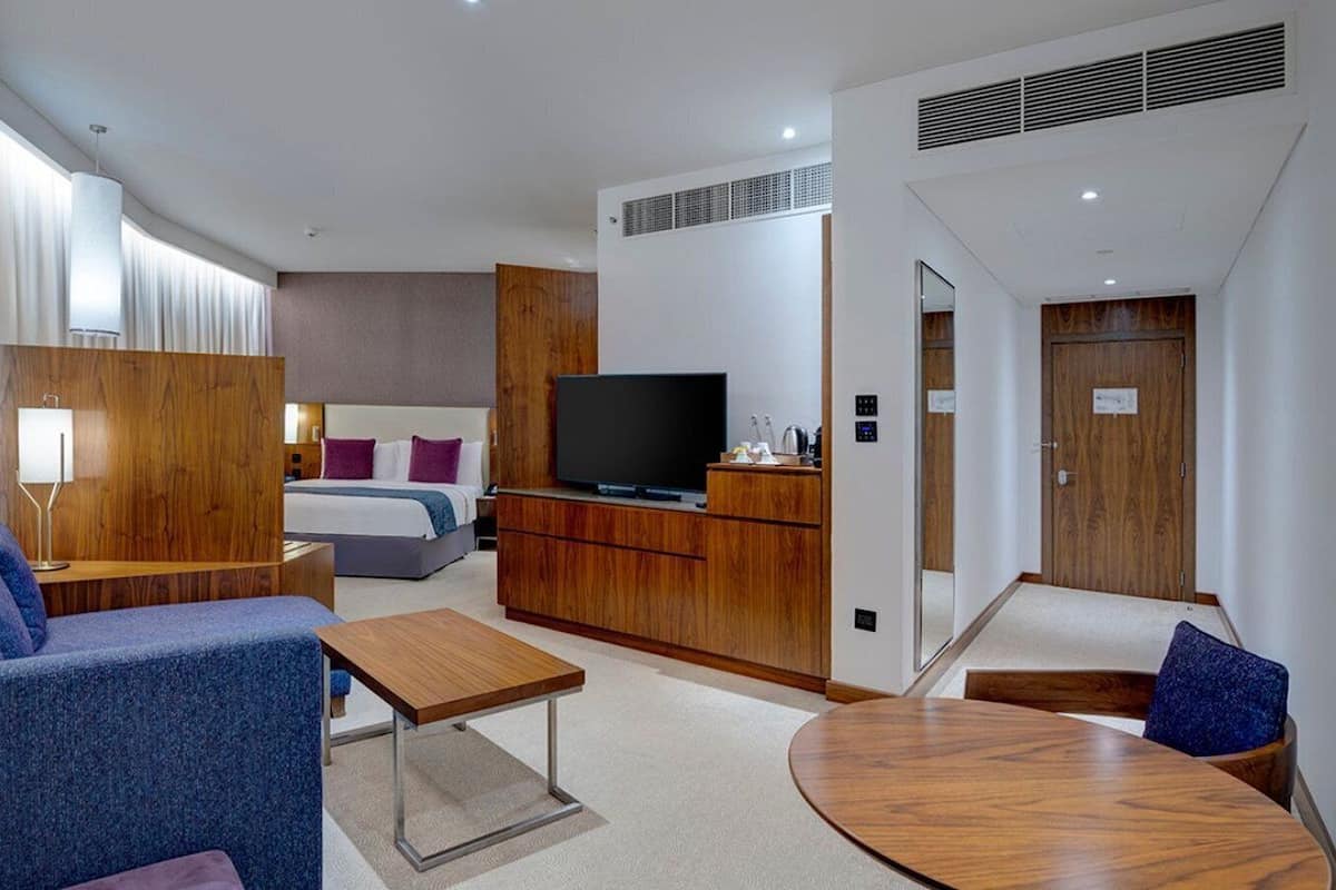 A modern hotel room with a sofa, a small table, a TV, a wooden cabinet, and a bed.