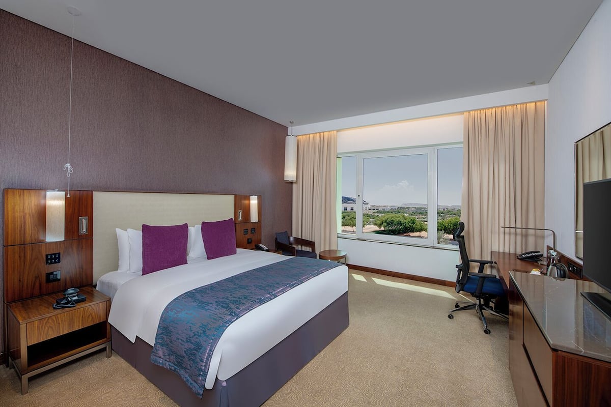A hotel room with a large bed, a desk, a chair, a TV, and a window with a view.