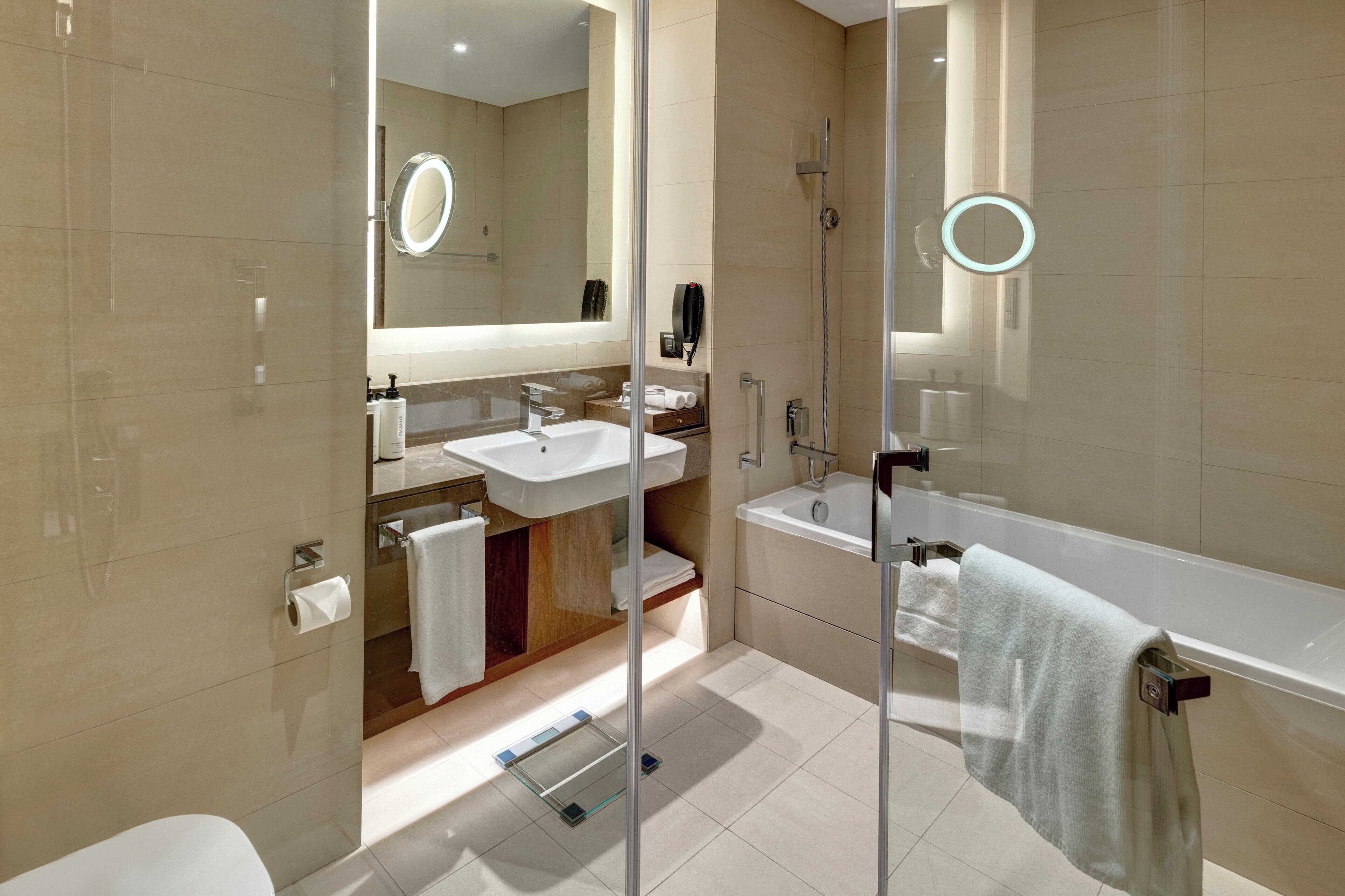 Ein modernes Badezimmer mit einer gläsernen Duschkabine, einem großen Spiegel und einer Badewanne.