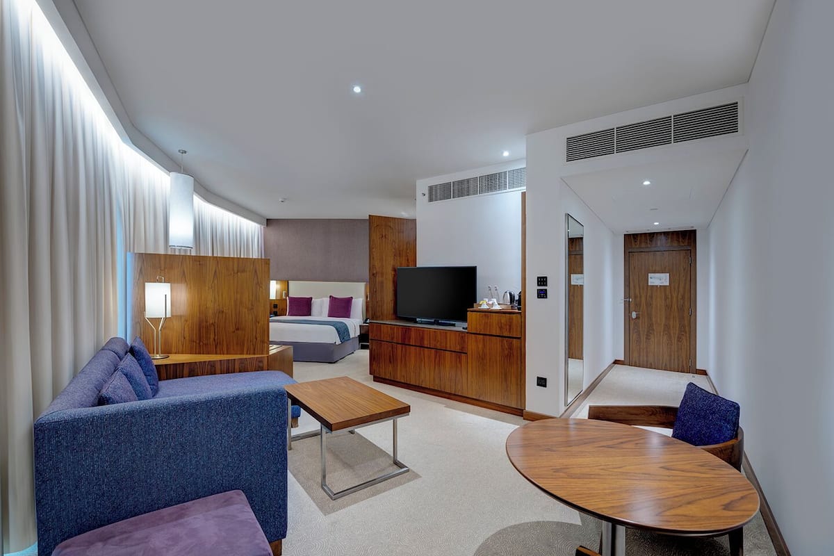 A modern hotel room with a sofa, a small table, a TV, a bed, and a desk.
