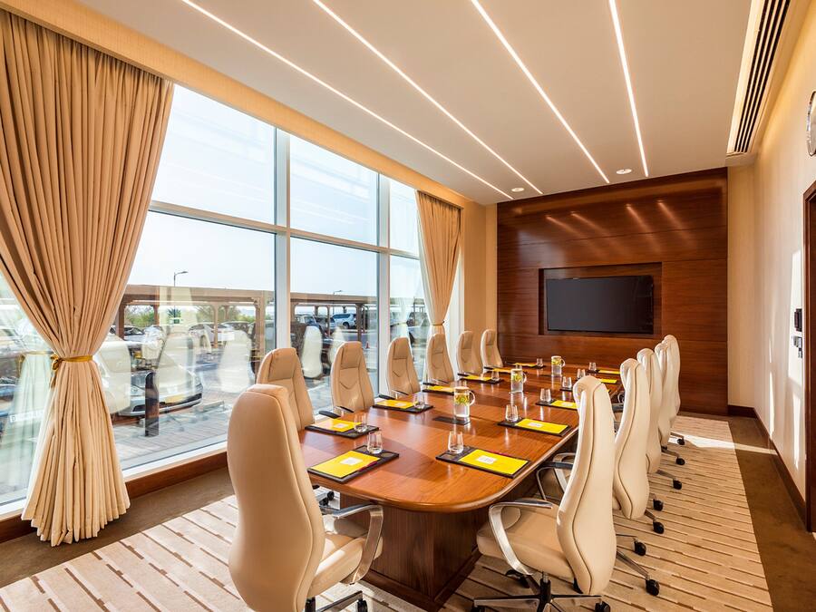 A conference room with a long table, chairs, a TV, and large windows with curtains.