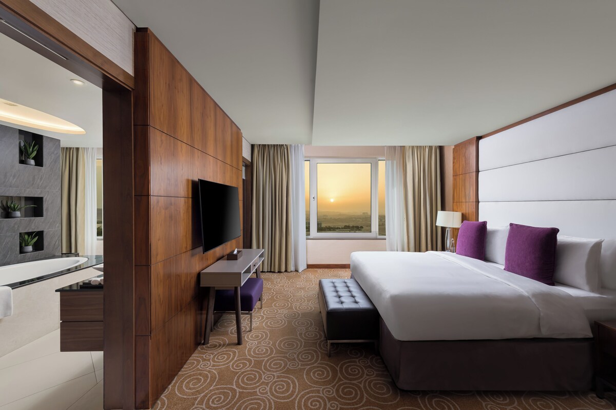 A hotel room with a bed, a desk, a television, and a window with curtains.
