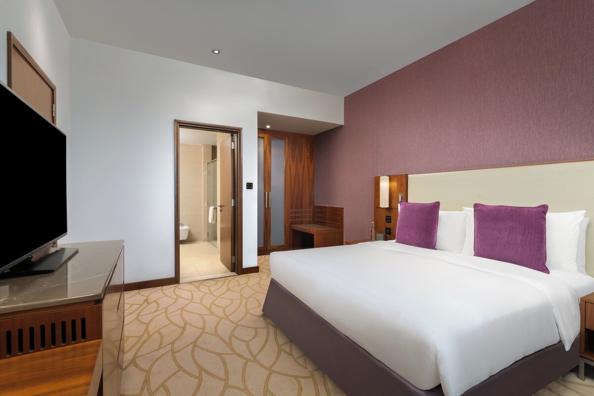 A hotel room with a bed, a television, a desk, and a bathroom visible through an open door.