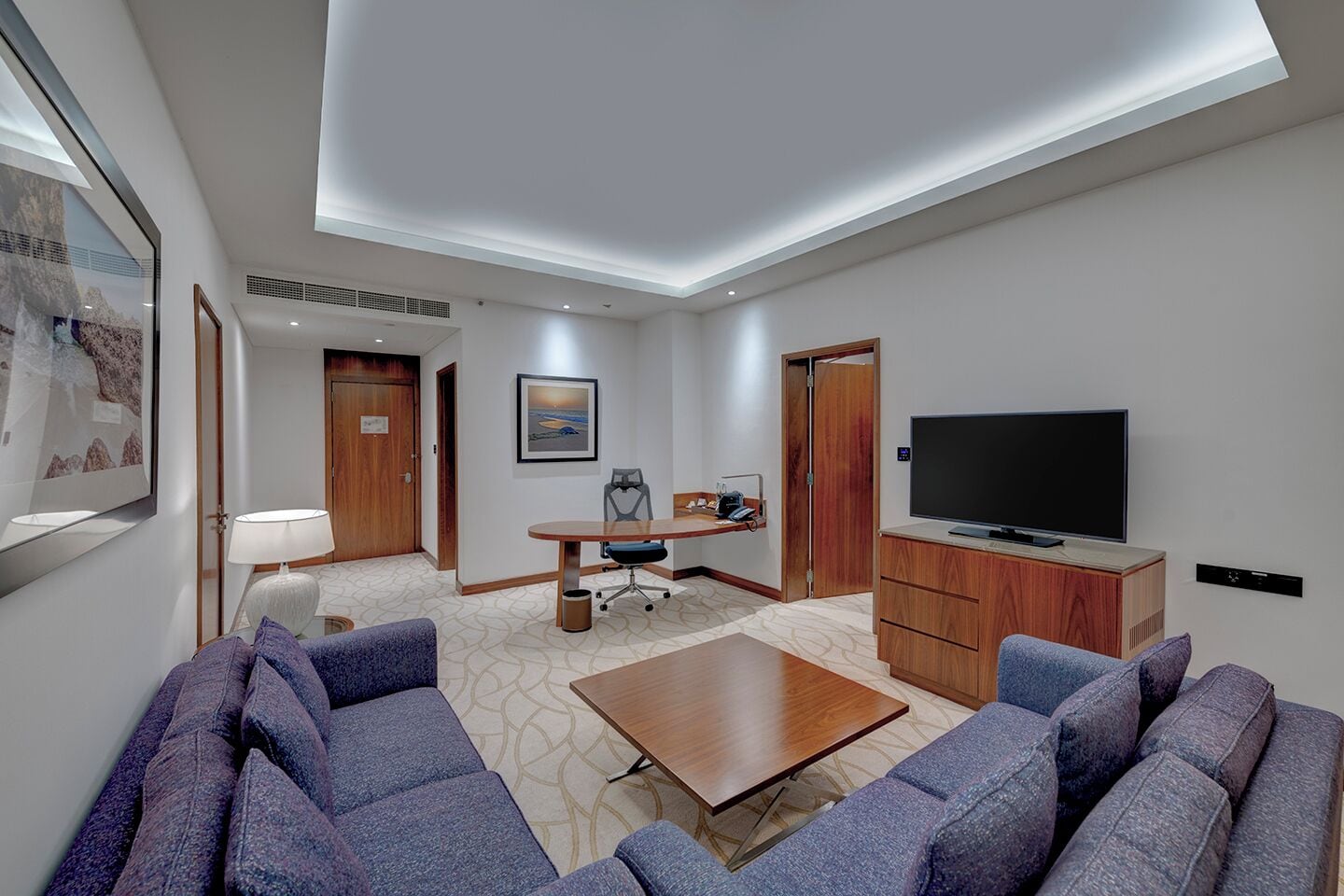 Une chambre d’hôtel dotée d’une grande télévision à écran plat, d’un ensemble de canapés, d’une table à manger et d’un tableau au mur.