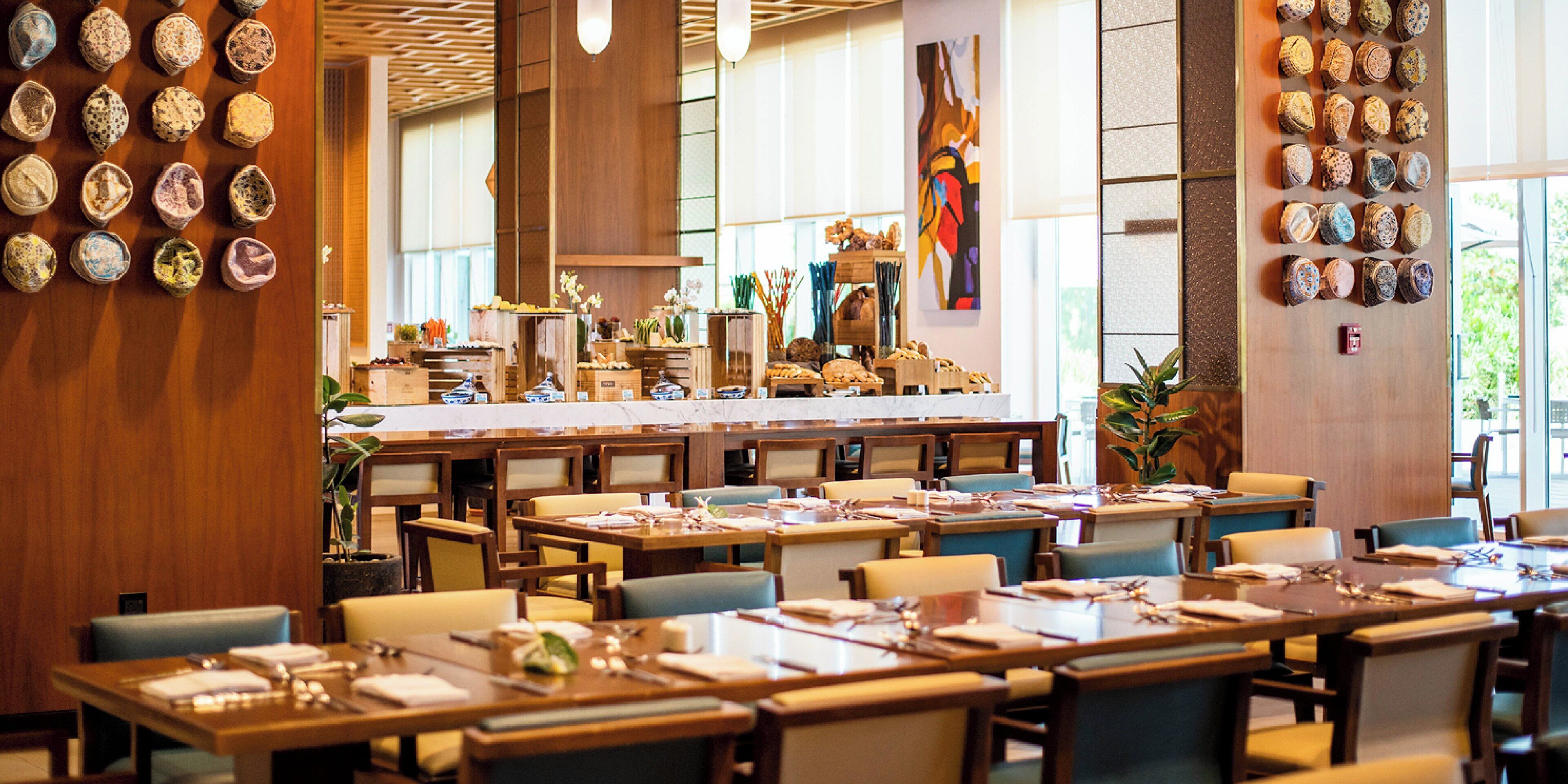 A restaurant with multiple dining tables and chairs, a long counter with food items, and a wall with decorative plates.