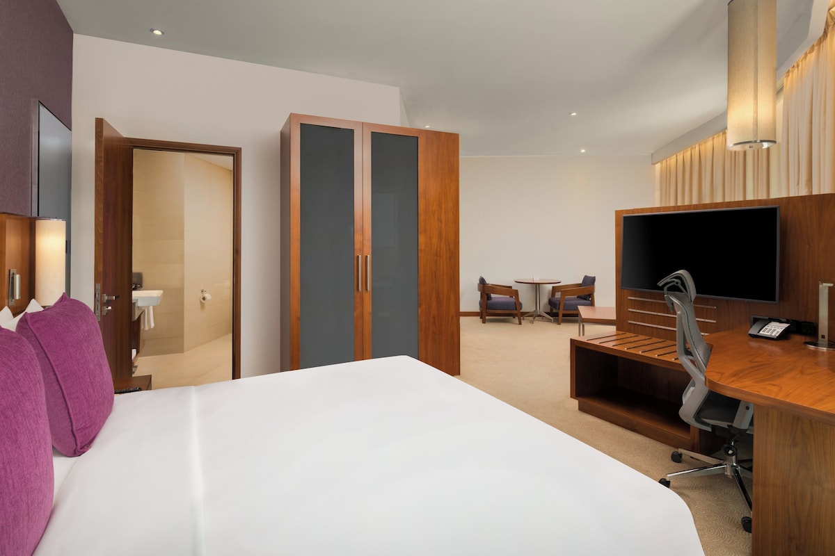 A hotel room with a large bed, a desk with a chair, a television, and a wardrobe.