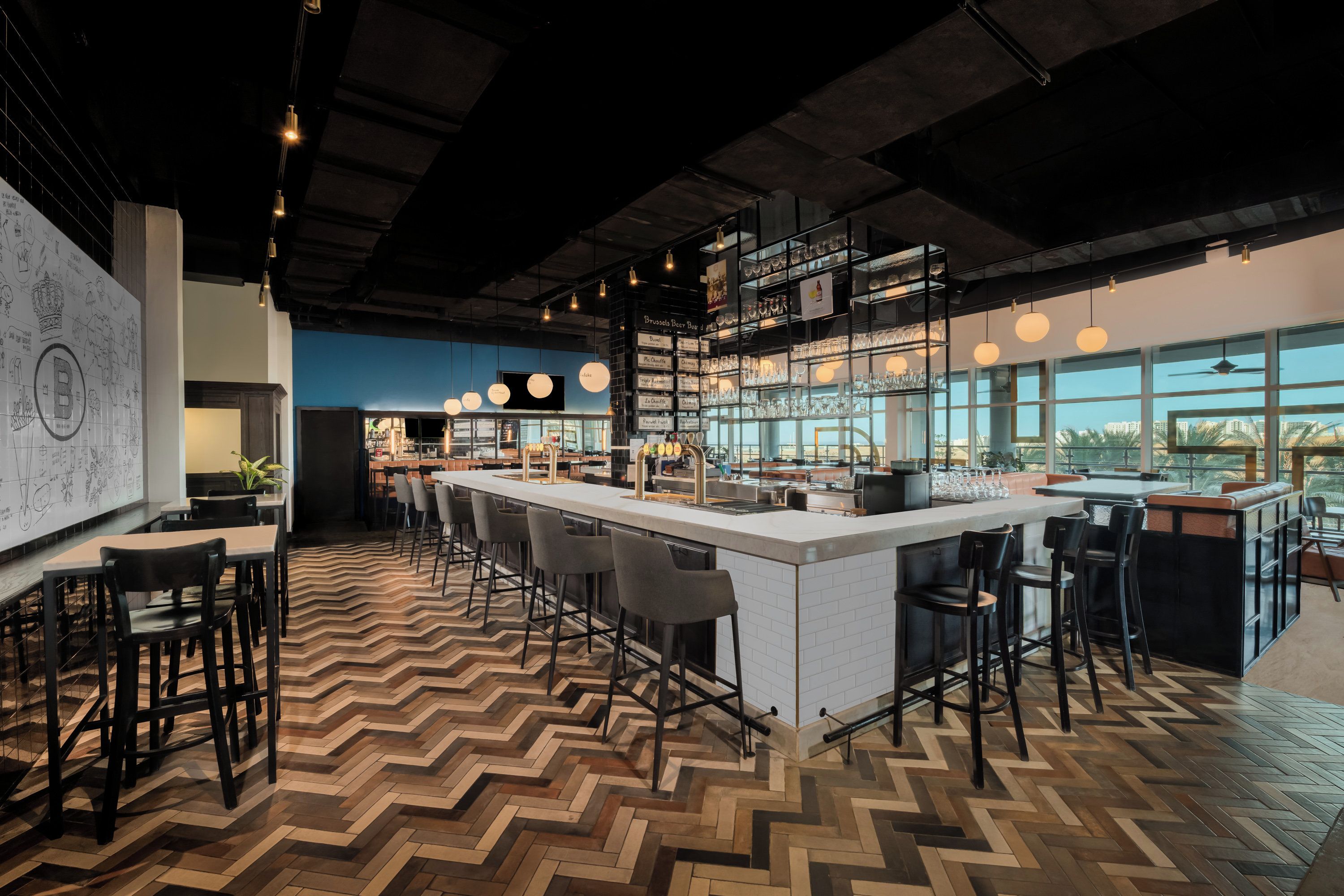 A modern bar area with a herringbone floor pattern, bar stools, and a large window offering a view of the cityscape.