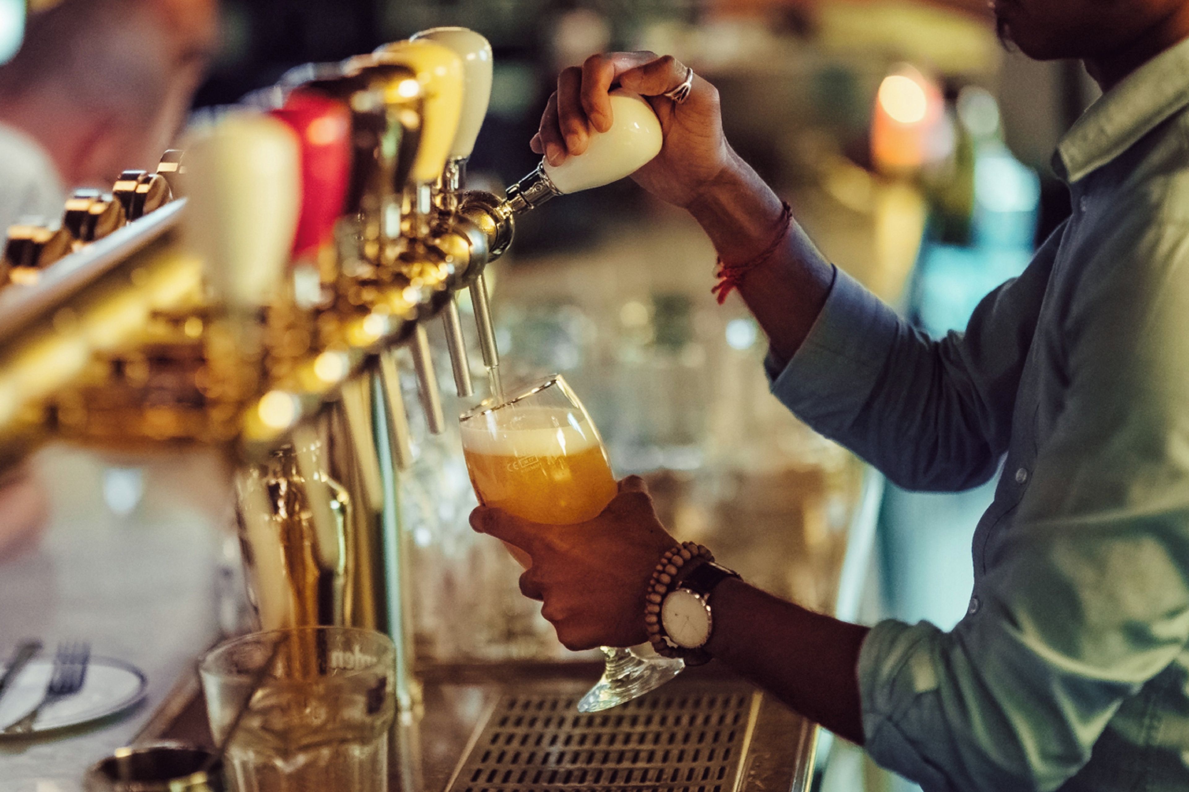 A person pouring a drink from a tap into a glass.