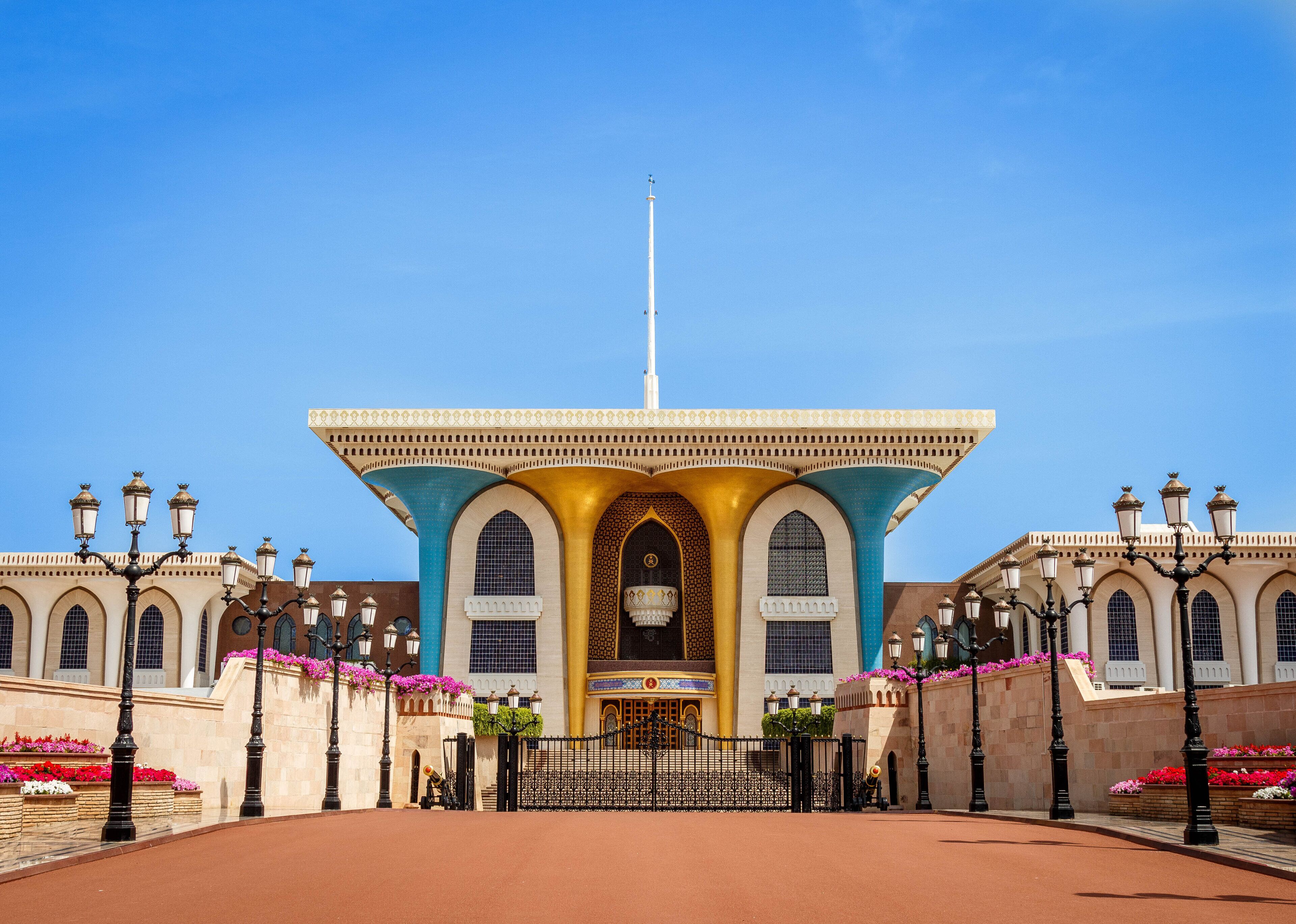 A large, ornate building with a central archway, flanked by symmetrical wings and a prominent flagpole.