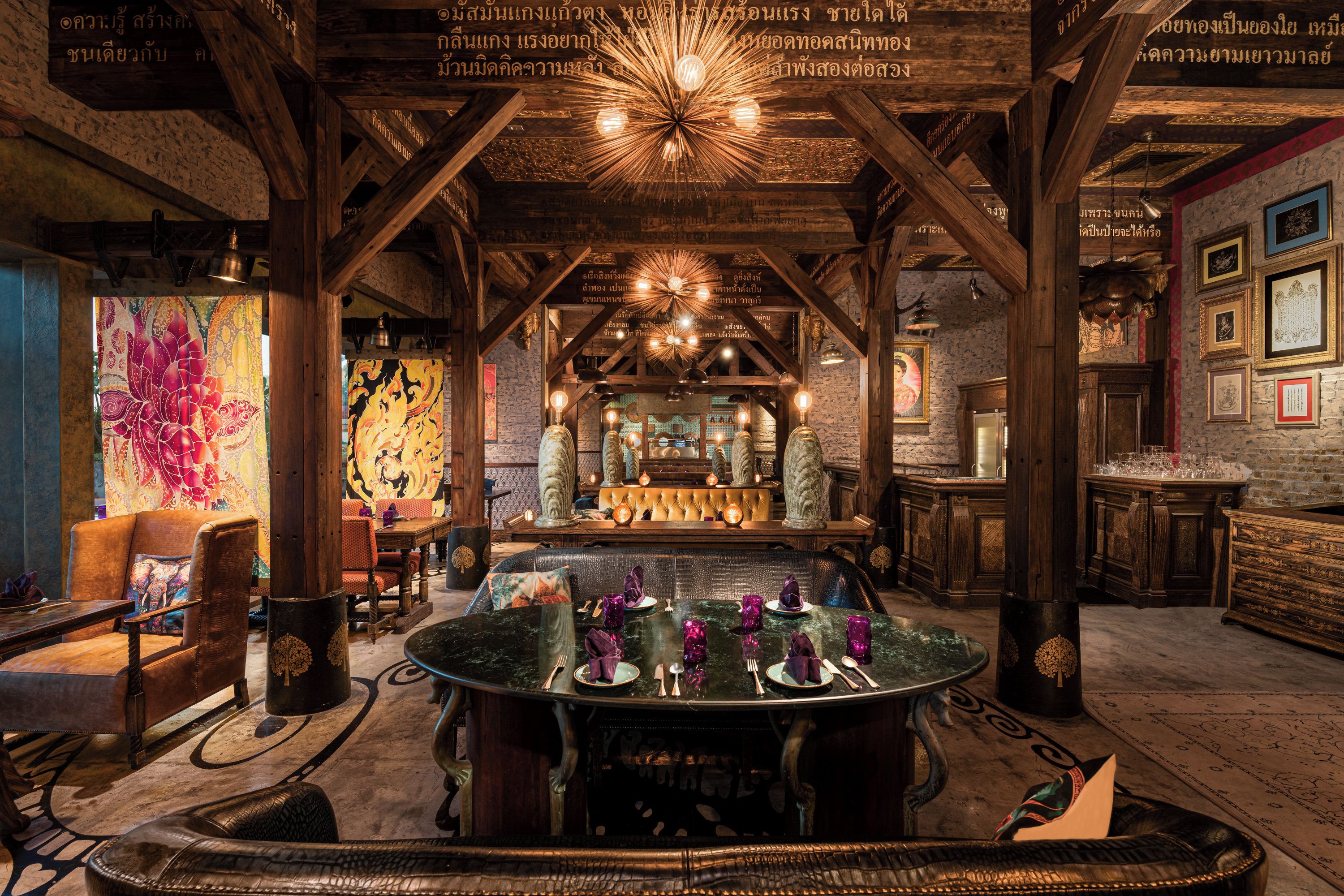 Une pièce avec une table centrale dressée pour le repas, des poutres en bois au plafond et divers tableaux encadrés accrochés aux murs.