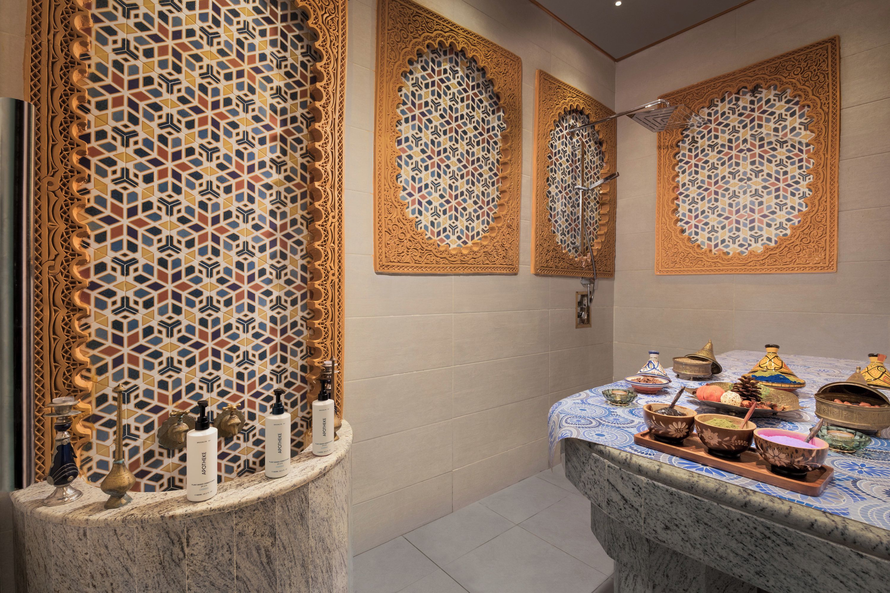 Une salle de bain avec des carreaux de céramique aux motifs complexes, un comptoir en marbre et une variété de produits de toilette.