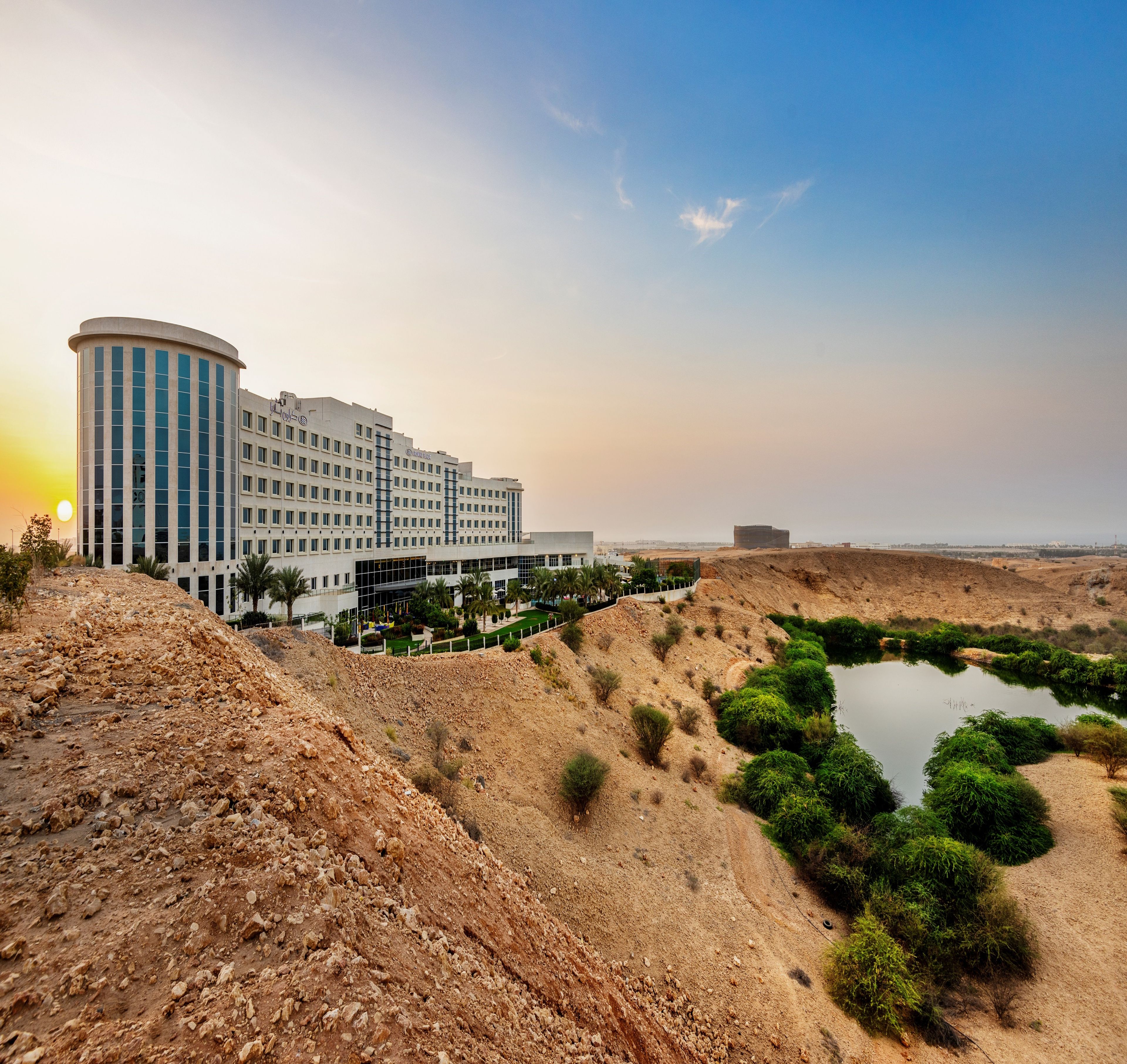 A modern hotel with a curved facade, a landscaped garden, and a small pond.