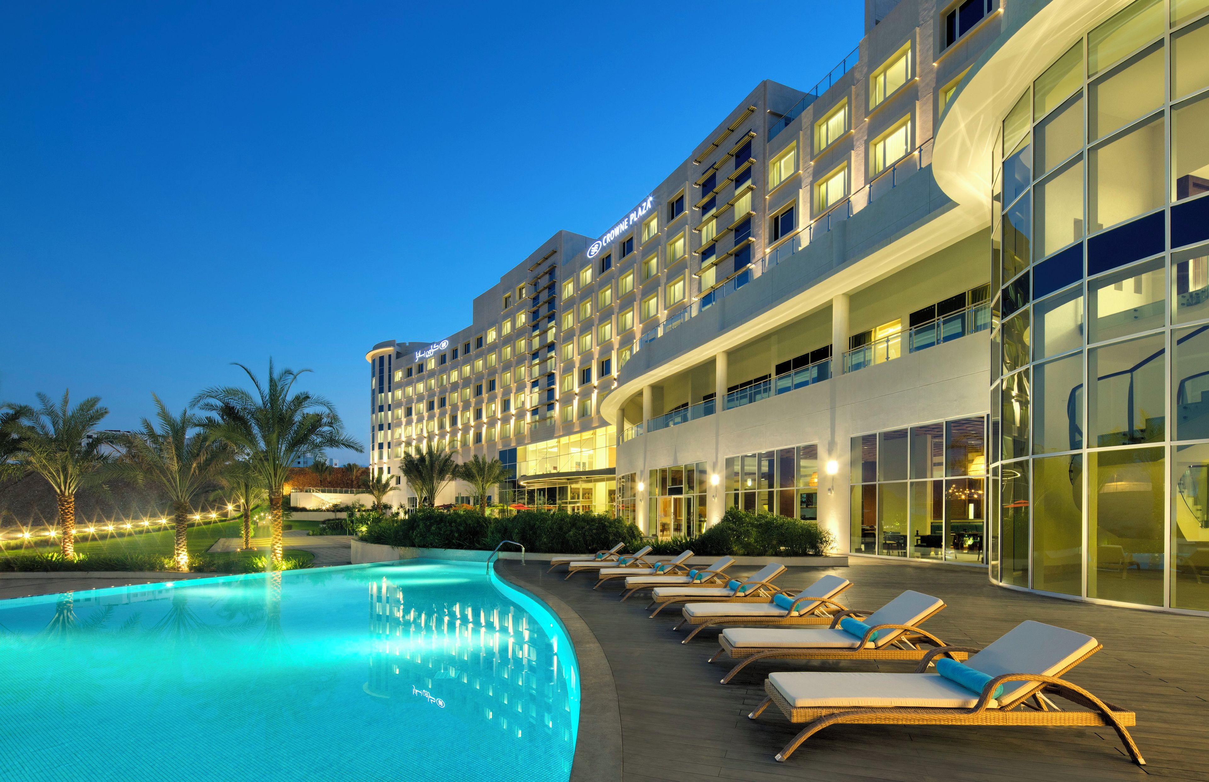 Un hotel con piscina, sillas de descanso y una fachada de edificio moderna.