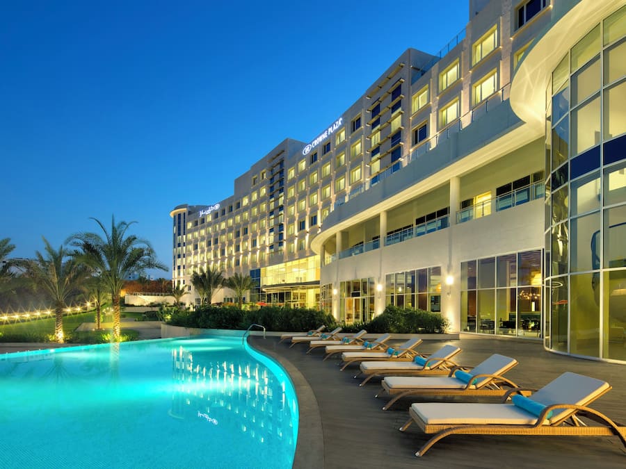 Un hotel con piscina, sillas de descanso y una fachada de edificio moderna.
