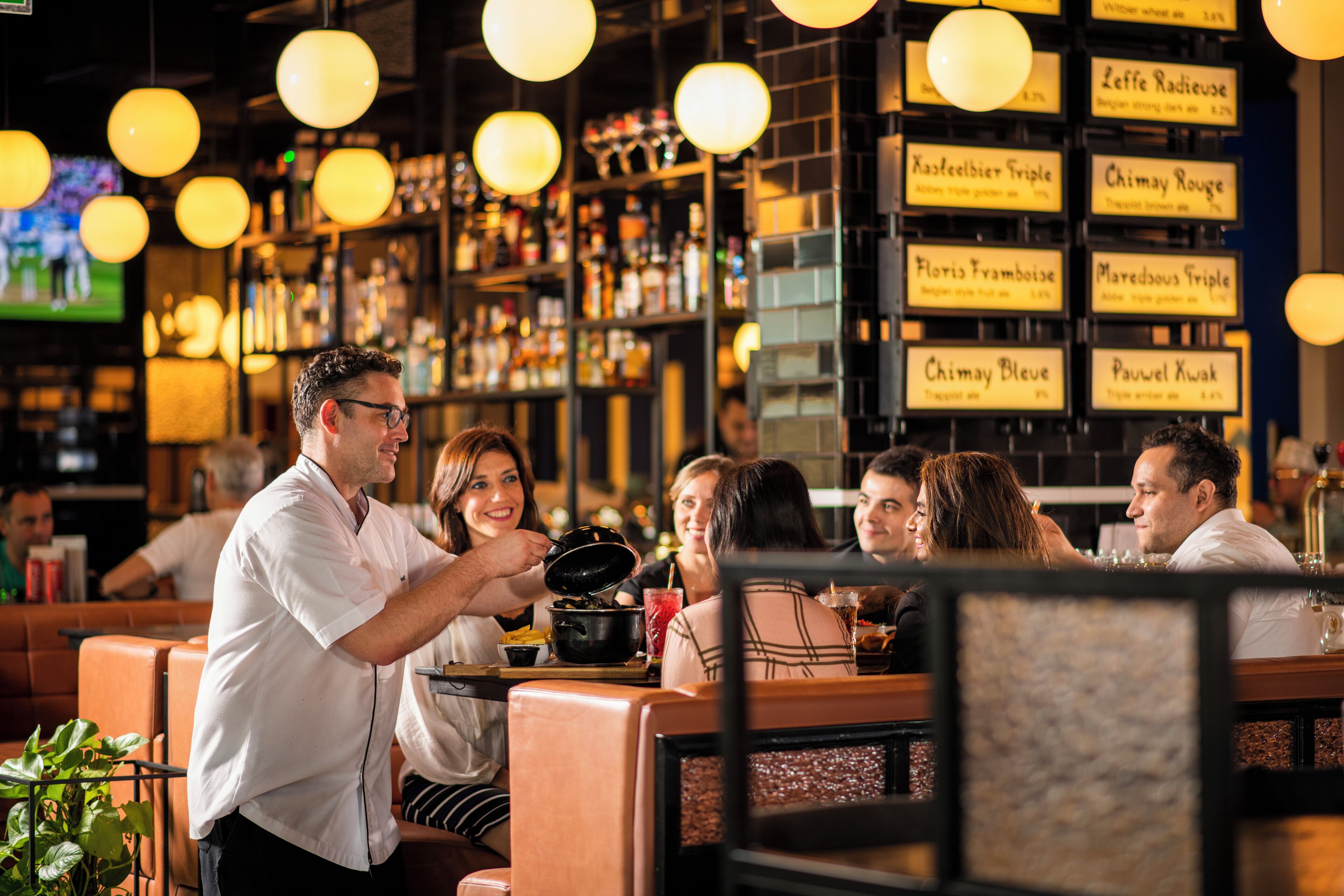 A bar with multiple seating areas, a bartender serving drinks, and a menu with various drink options.