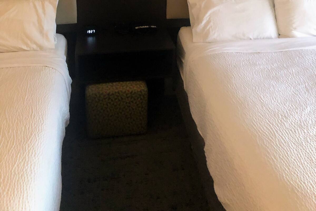 Ein Hotelzimmer mit zwei Einzelbetten, einem Nachttisch und einem kleinen Tisch mit zwei Lampen.