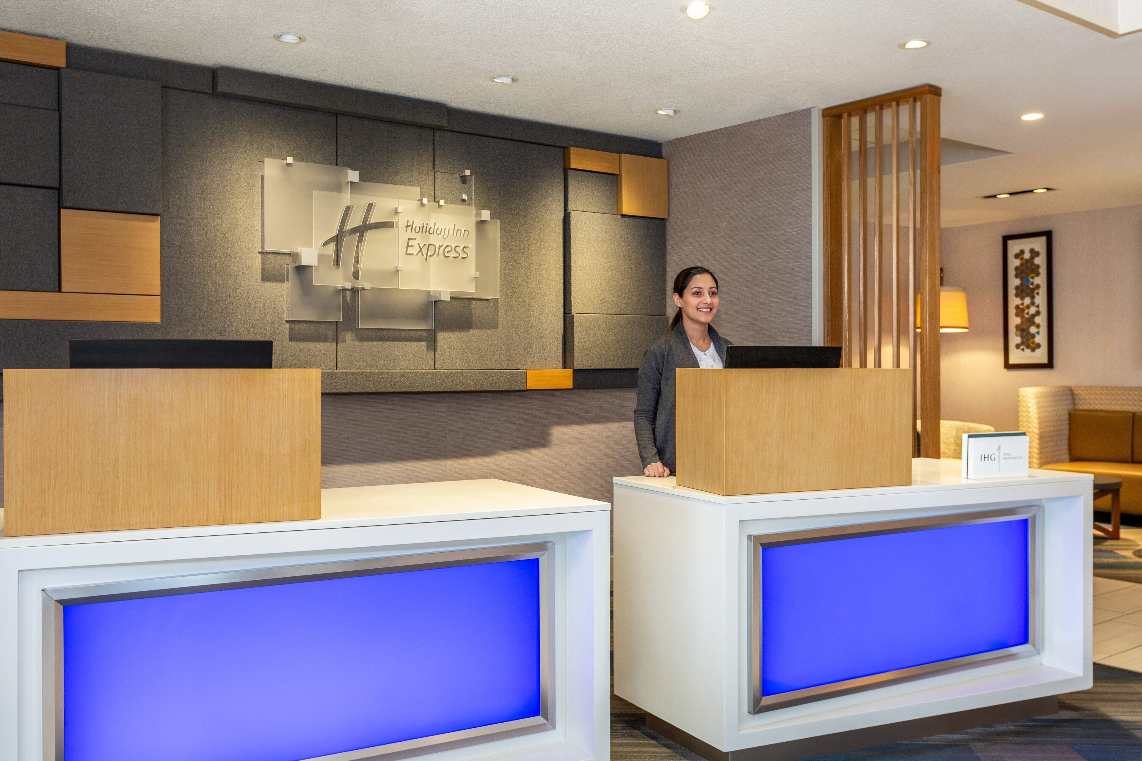 Vastaanottotiski, jossa on «Holiday Inn Express» -kyltti, puinen sermi ja sinisellä valolla taustavalaistu näyttö.