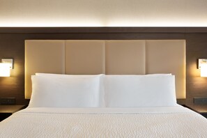 A neatly made bed with white linens and a headboard with built-in lighting.