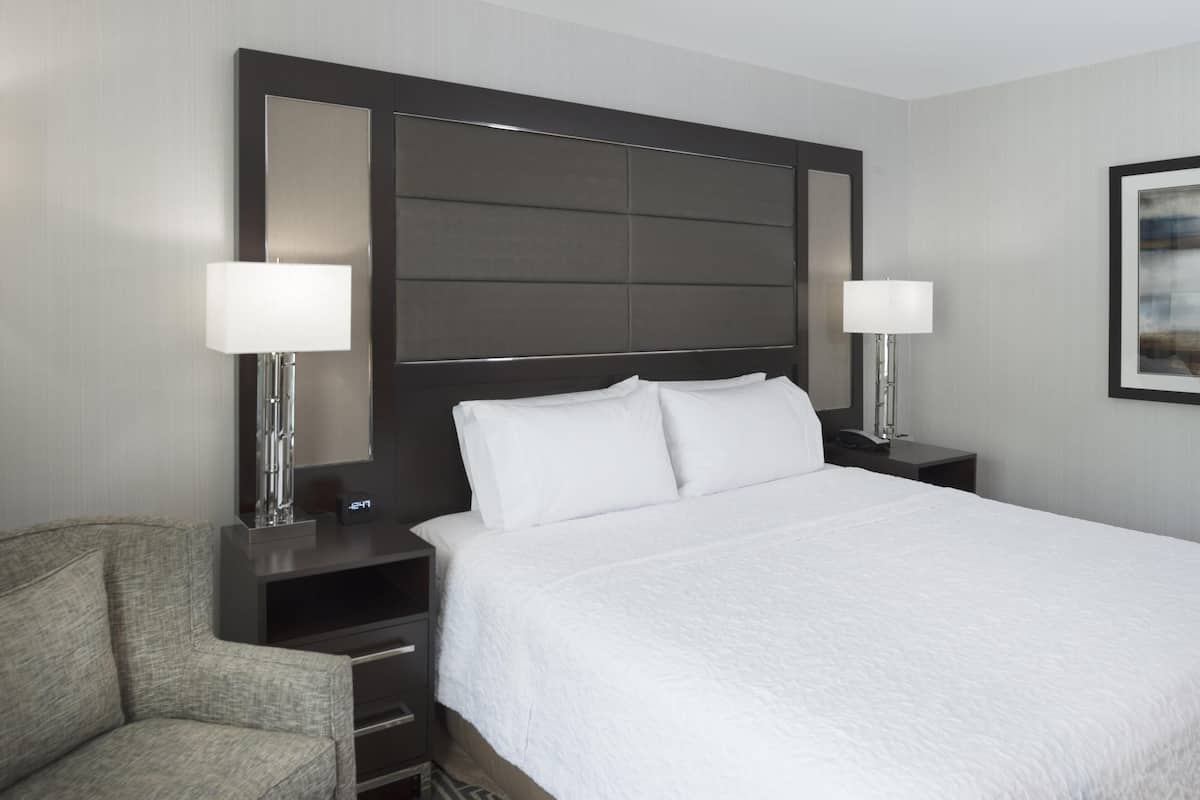Quarto de hotel com uma cama grande, duas luminárias de cabeceira, uma cadeira e uma mesa de cabeceira.
