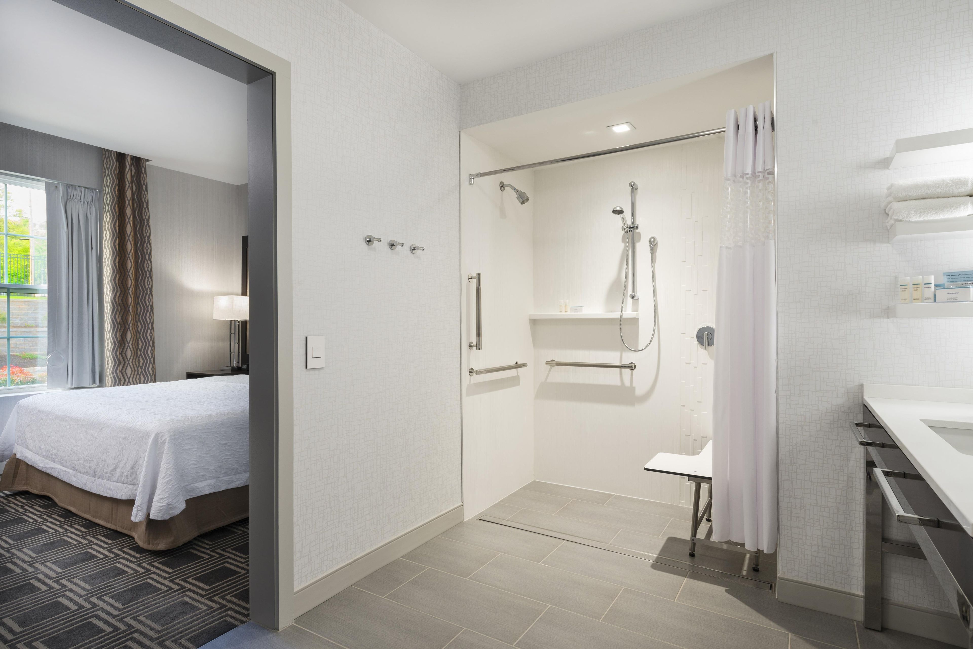 Ein Hotelzimmer mit einem Bett, einer Dusche und einem Badezimmer mit Waschbecken und Handtuchhalter.