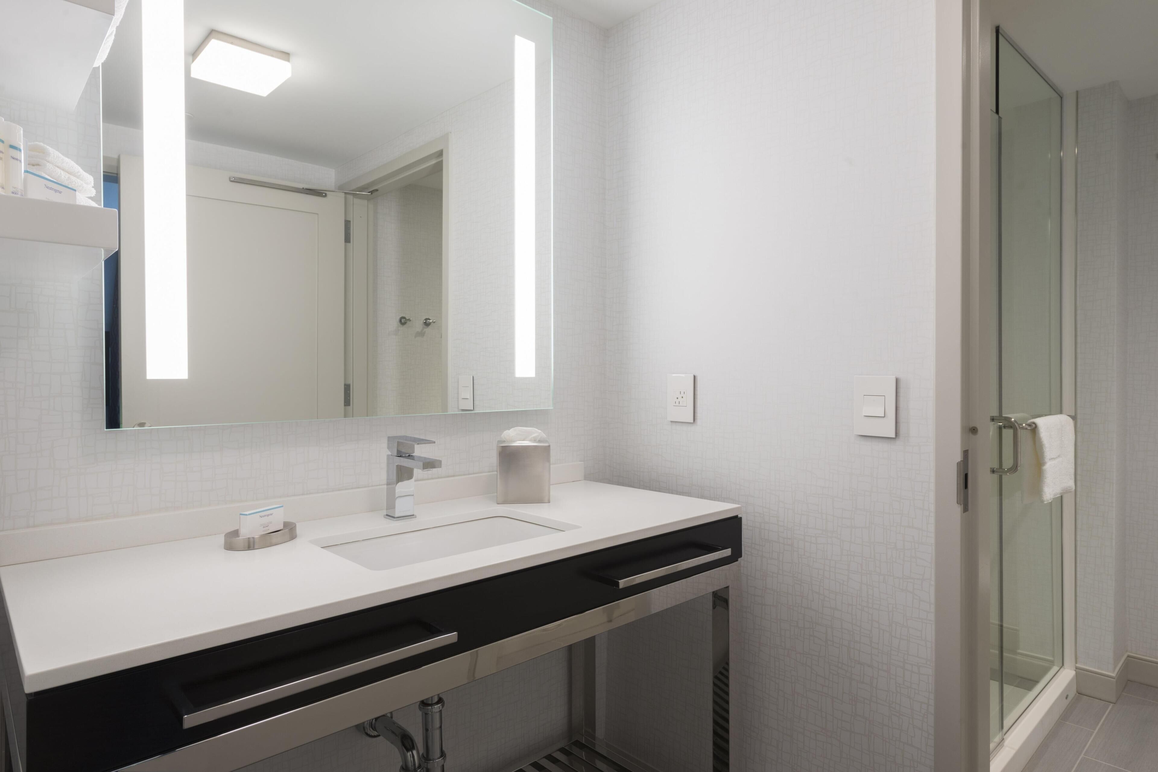 A modern bathroom with a white sink, mirror, and glass shower enclosure.