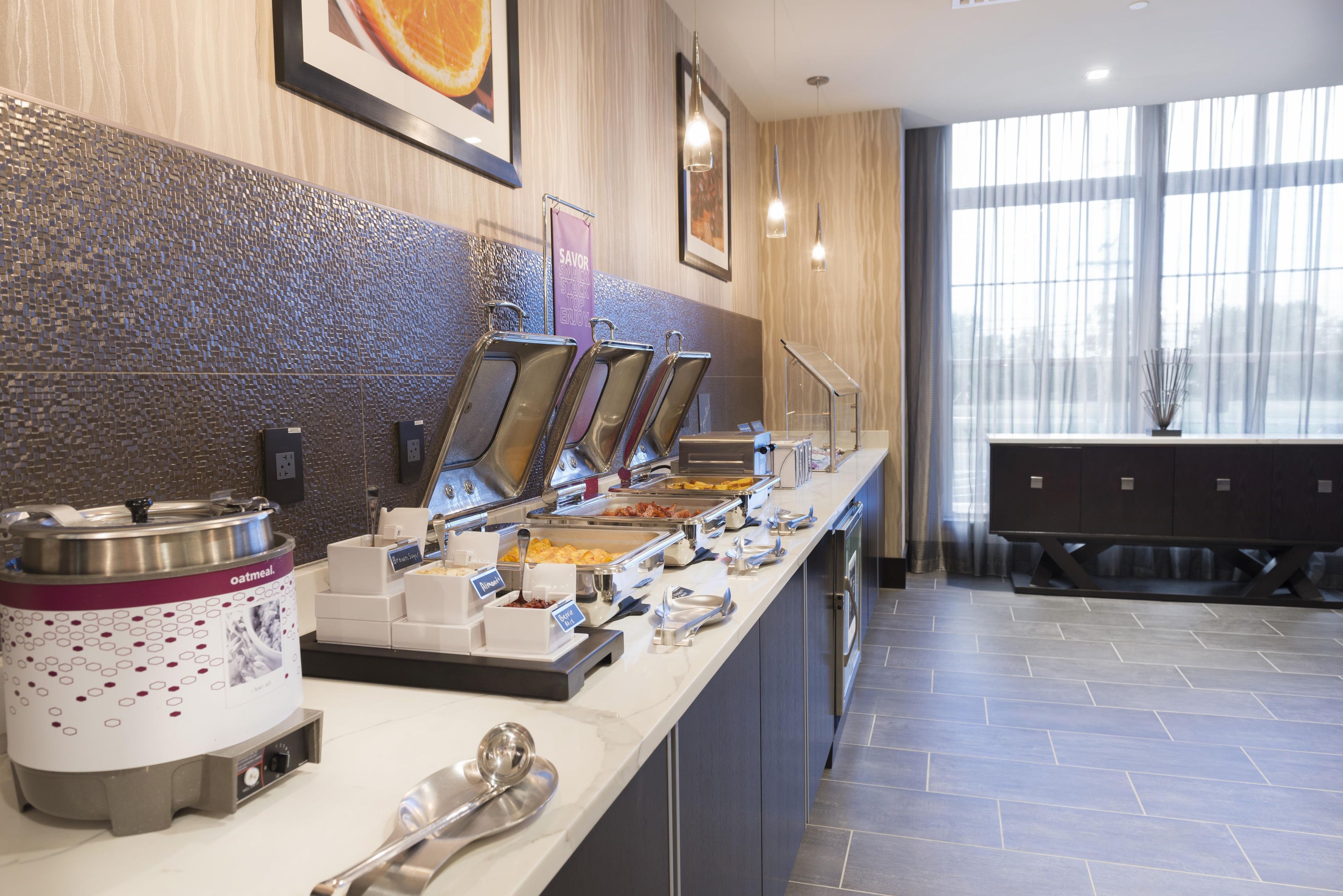 A buffet area with various food stations, a coffee machine, and a seating area with a view of the outdoors.