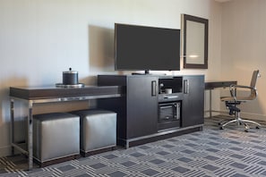 A modern hotel room with a flat-screen TV, a minibar, a built-in oven, and a seating area with a chair and ottoman. - Hampton Inn & Suites Bridgewater (Bridgewater)