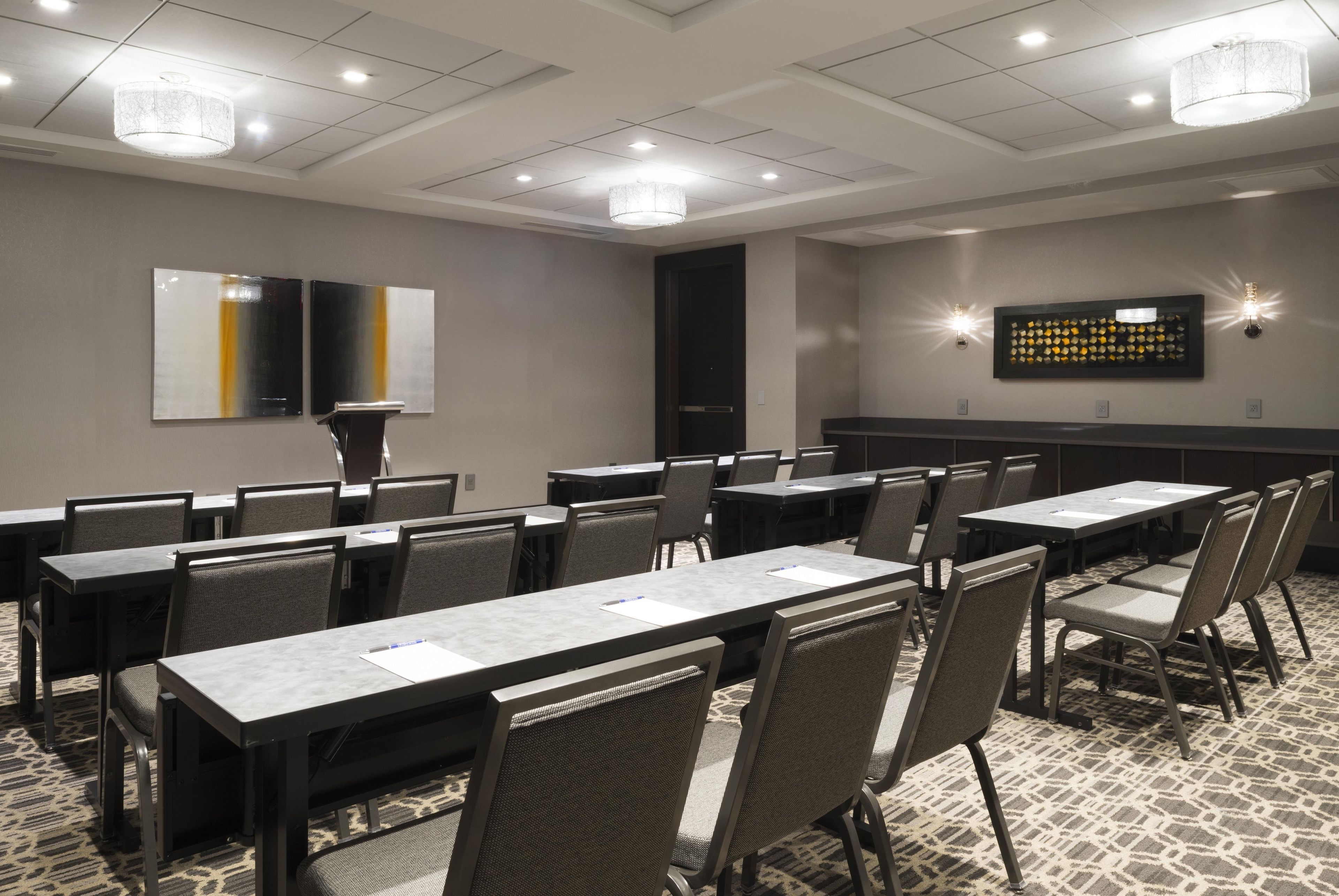 A conference room with multiple tables and chairs, a chandelier, and wall-mounted lighting.