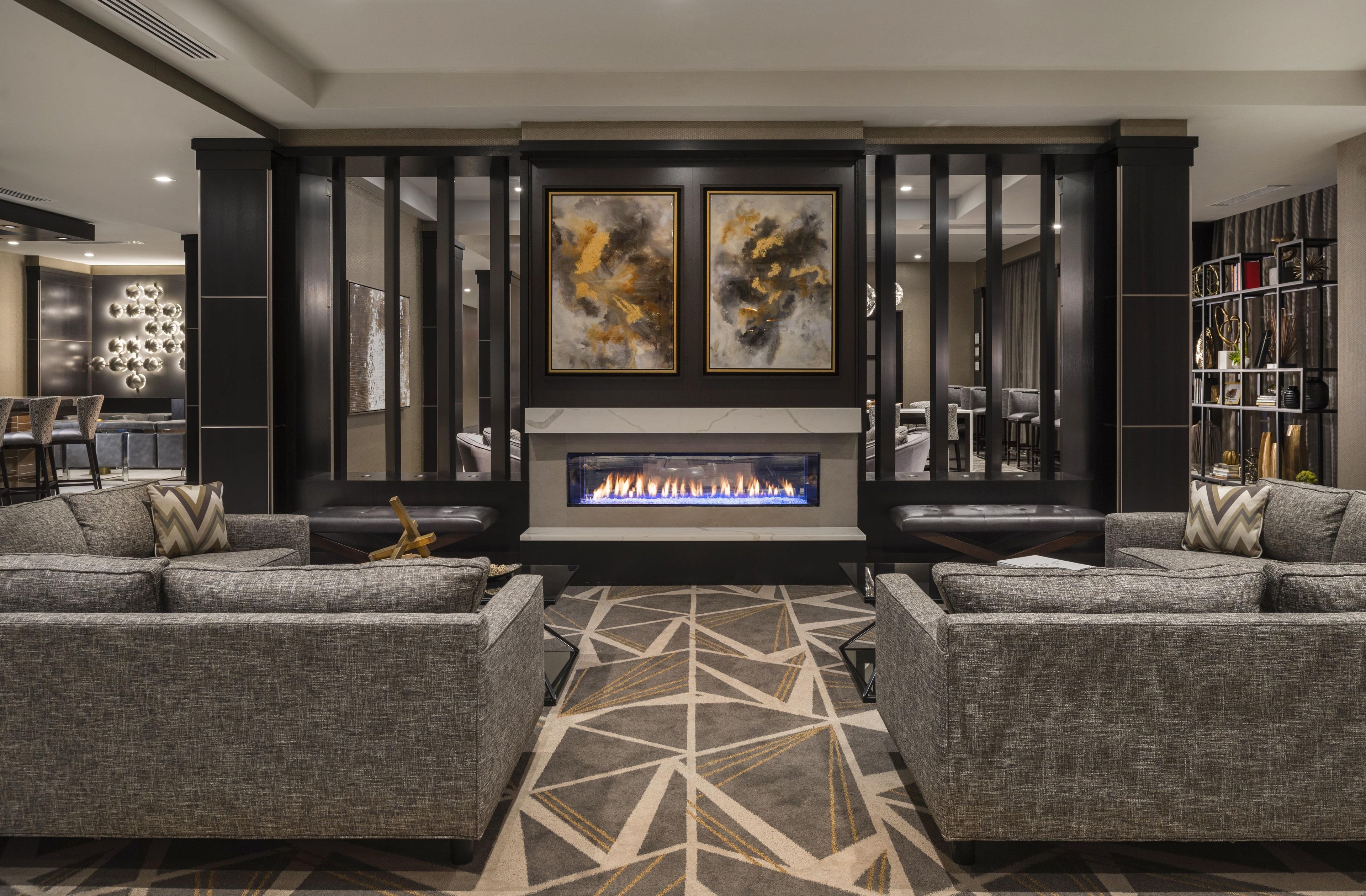 A modern living room with a fireplace, grey sofas, a patterned rug, and abstract art on the wall.