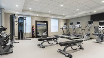Ein Fitnessstudio mit Laufbändern, Kraftgeräten und einer Spiegelwand.