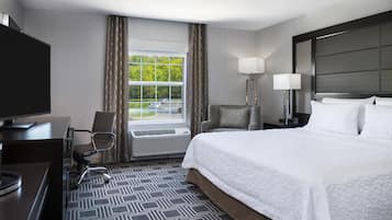 A hotel room with a bed, a desk, a chair, a TV, a window with curtains, and a view of the outdoors.