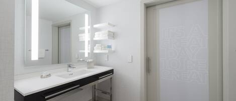 Un baño moderno con un espejo grande, tocador blanco y una cita motivacional enmarcada en la pared.
