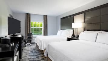 A hotel room with two beds, a desk with a TV, a chair, and a window with curtains.