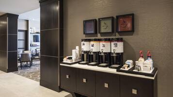 A hotel room with a coffee station, a seating area, and a view of the hallway.