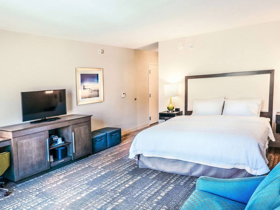 A hotel room with a bed, a TV, a desk, a chair, and a lamp.