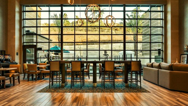 A spacious indoor area with a large window, a wooden floor, and a seating area with chairs and a sofa. - Hampton Inn & Suites Mission Viejo (Mission Viejo)
