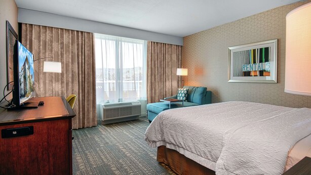 A hotel room with a bed, a desk with a TV, a chair, a lamp, and a window with curtains. - Hampton Inn & Suites Mission Viejo (Mission Viejo)